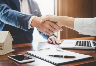 Business Handshake Symbolizing a Successful Deal Close-up of a handshake between two business professionals at a desk with a contract, pen, laptop, and smartphone, symbolizing a successful deal.